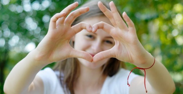 A young teenage girl making a heart shape with her hands and smiling through the gap