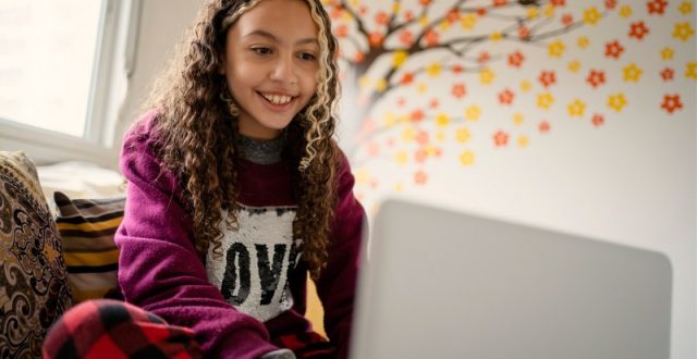 A happy teenage girl in a red hoodie using a laptop