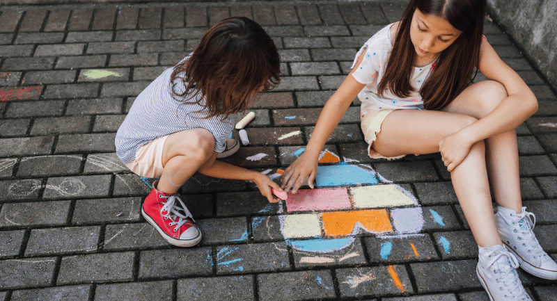 Children drawing colourful heart shape with chalk on a brick pavement.