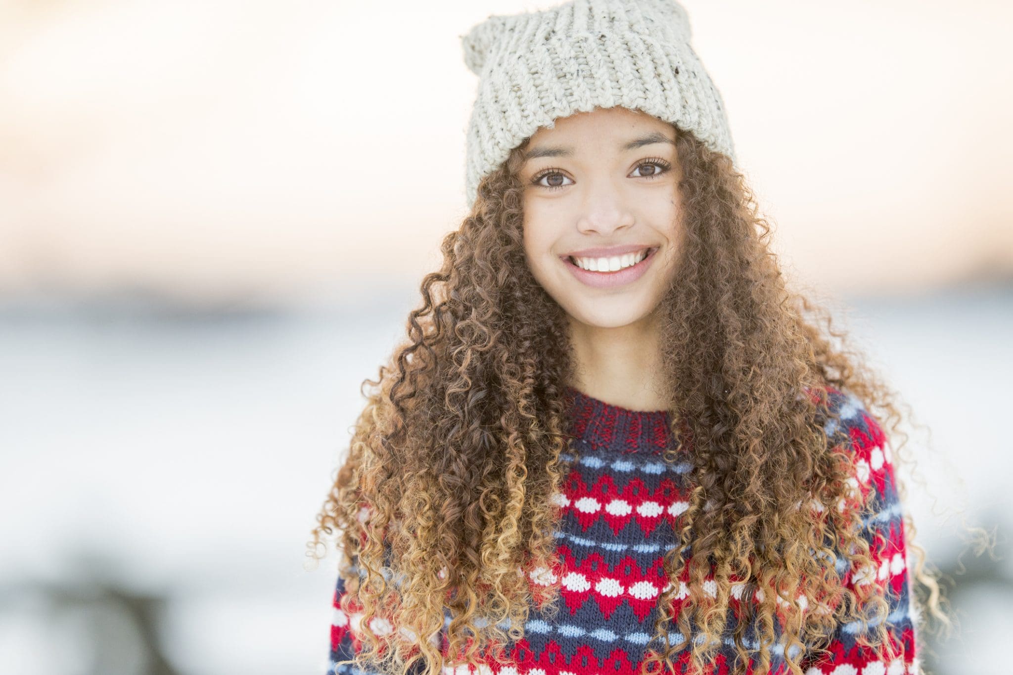 A portrait of a beautiful mixed race teenager enjoying her time outside during winter time. She wears warm clothing and a winter hat.